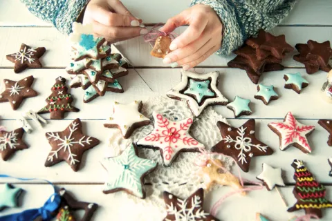 A table full of decoarted gingerbread cookies. two hands decorate a bell shaped cookie