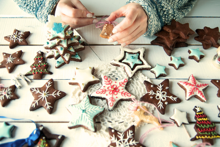 A table full of decoarted gingerbread cookies. two hands decorate a bell shaped cookie
